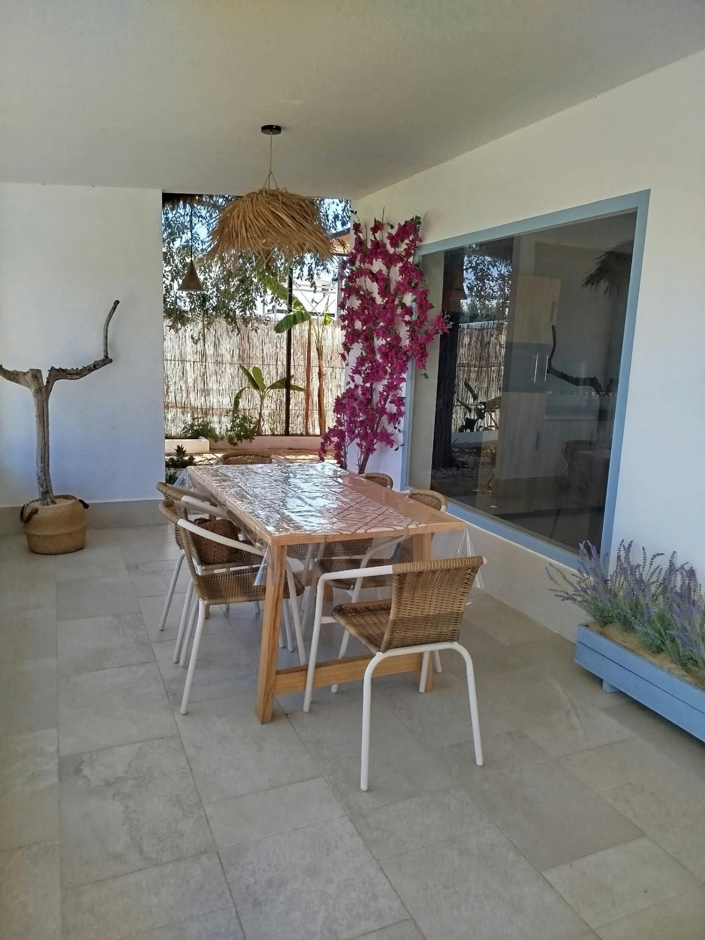 Porche con mesa de madera, sillas de mimbre y buganvilla